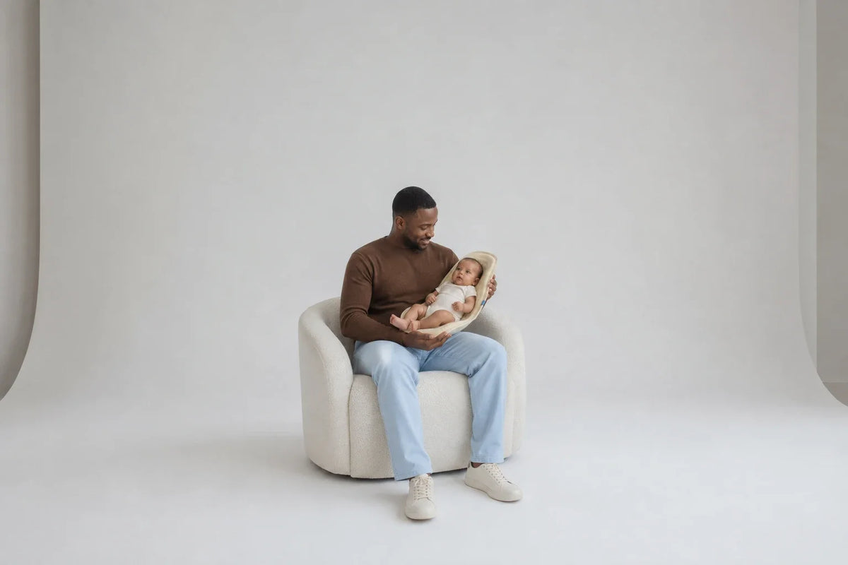 A seated father keeping both hands around baby and Nido