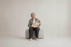 A seated grandmother supporting a baby with Nido in her arms