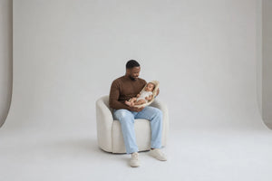 A seated father keeping both hands around baby and Nido