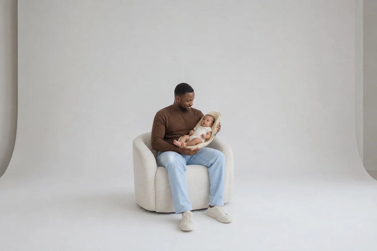 A seated father cradles his awake baby in Nido, supporting the pod with both arms